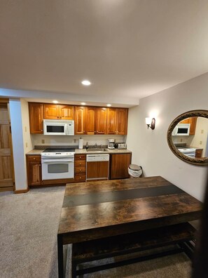 Une cuisine avec des meubles de rangement en bois, un four à micro-ondes blanc, une cuisinière, un lave-vaisselle et une table à manger.