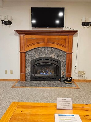 A fireplace with a television above it, a sign indicating a gas fireplace, and a table with a sign in front. - Ski-in/Ski-out Studio on Okemo Sachem Trail (Ludlow)