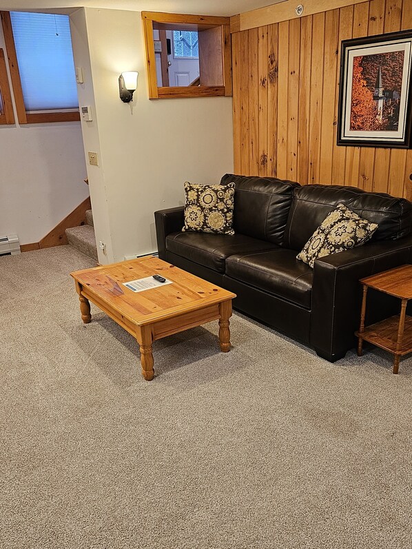 A living room with a black leather sofa, two patterned throw pillows, a wooden coffee table, and a framed picture on the wall. - Ski In/Out Studio at Okemo on Sachem Trail (Ludlow)