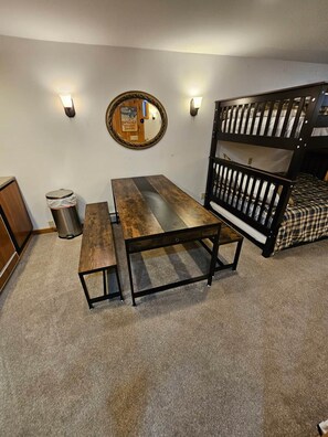 A bunk bed with a wooden frame and a mattress, a wooden table with a bench, a trash can, and a wall-mounted mirror. - Ski-in/Ski-out Studio on Okemo Sachem Trail (Ludlow)