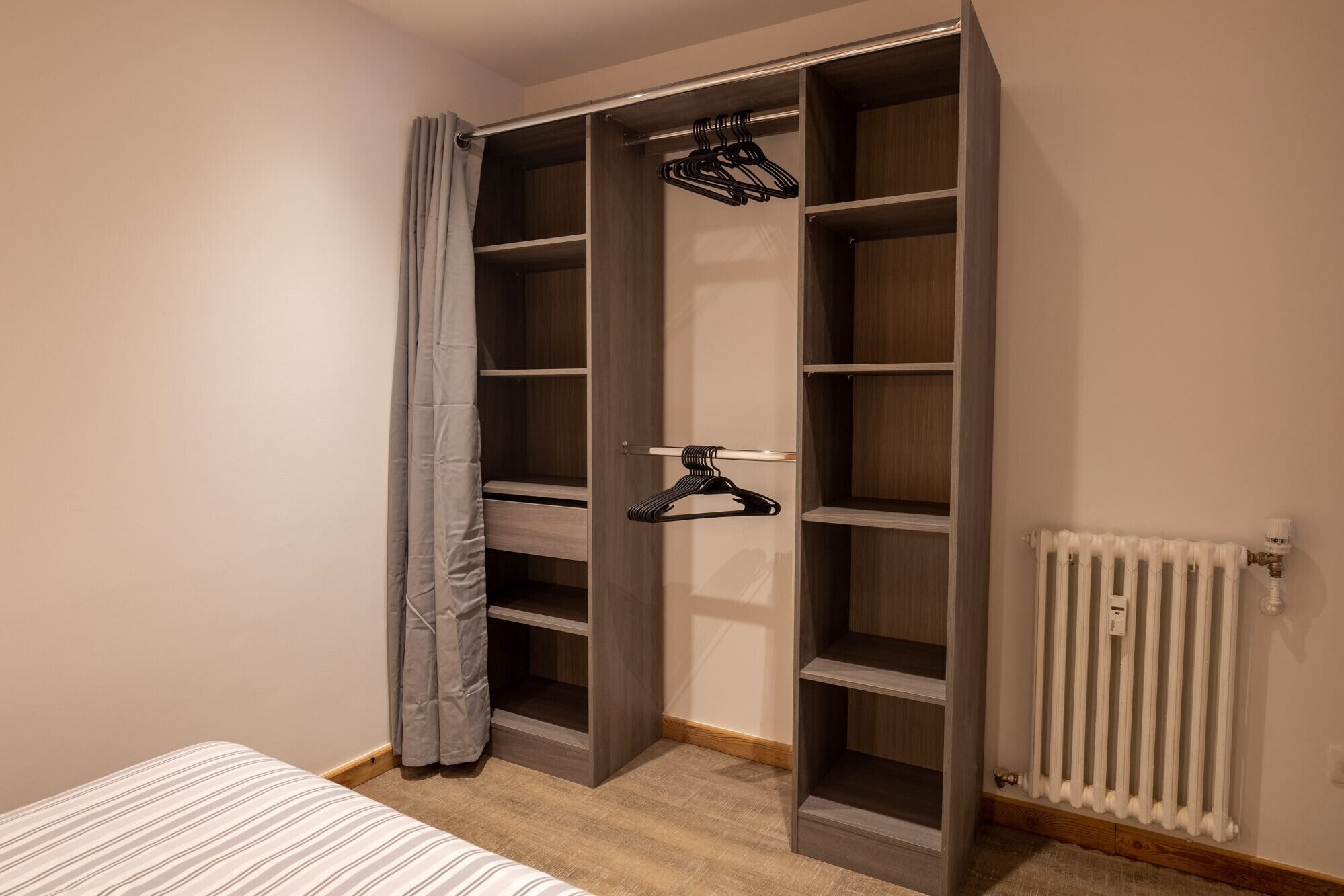A walk-in closet with multiple shelves and hanging space, a radiator, and a bed with striped bedding.