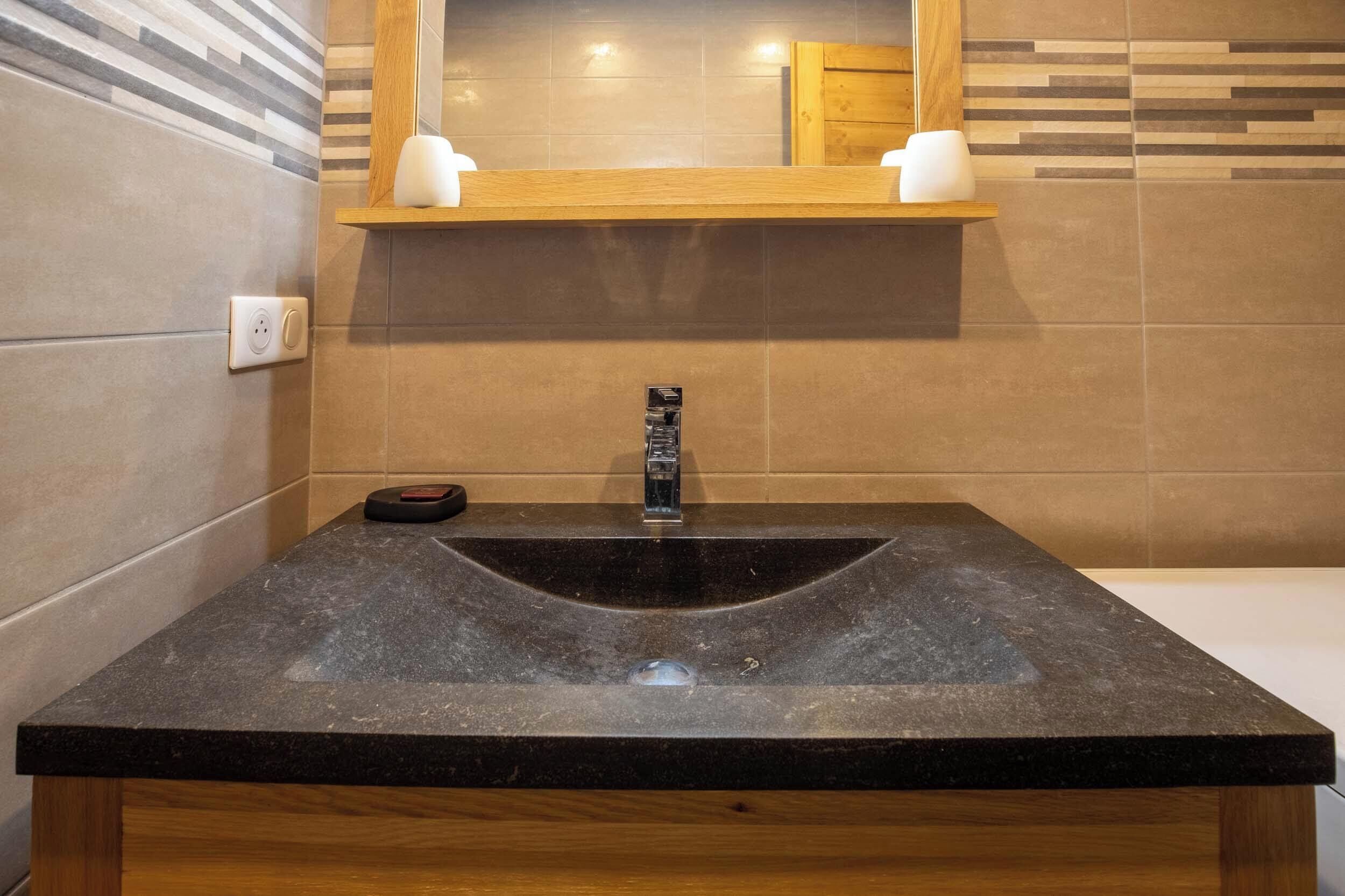 Ein Badezimmer mit einem schwarzen Granittisch, einer Holzwaschkabine und einem Spiegel über dem Tisch.