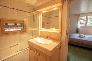 Un baño con bañera, lavamanos y ducha. Hay una ventana con vistas al exterior.