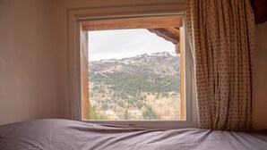 Ein Schlafzimmer mit einem großen Fenster und Blick auf eine gebirgige Landschaft.