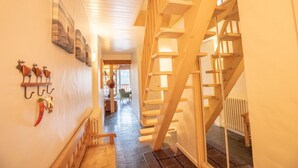 Eine Holztiefe, die zu einer zweiten Etage führt, ein Korridor mit Heizkörper und eine Wand mit Wanddekorationen.