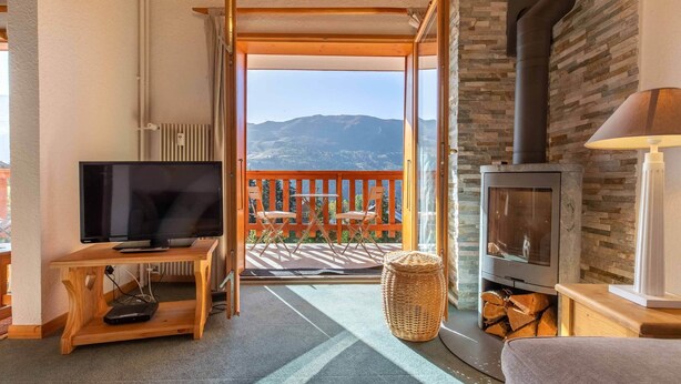Een gezellige kamer met een televisie, een open haard, een balkon met stoelen en uitzicht op bergen.