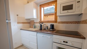 Een compacte keuken met witte apparaten, een houten raam en een betegelde spatwand.