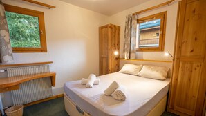 Een slaapkamer met een bed, een houten bureau, een radiator en een raam met uitzicht op groen.
