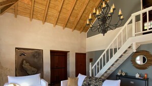 A spacious living room with a high wooden ceiling, a chandelier, and a staircase leading to an upper level.