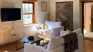 A spacious living room with a white sofa, a wooden ceiling, a TV mounted on the wall, and a large painting.