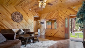 A wooden interior with a large clock, a sofa, and a staircase leading to a door. - Dog Friendly, Fully Gated, Private Cabin by Fool Hollow Lake (Show Low)