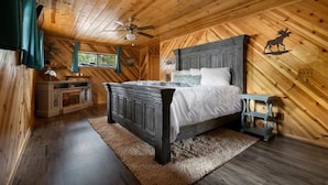 A wooden cabin bedroom with a bed, a nightstand, a dresser, and a ceiling fan. - Dog Friendly, Fully Gated, Private Cabin by Fool Hollow Lake (Show Low)