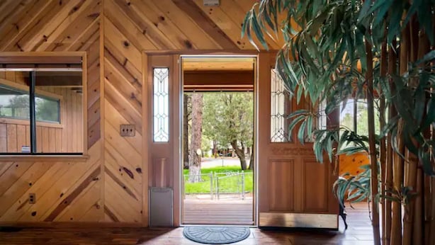 A wooden interior with a door leading outside, a window, and a plant. - Dog Friendly, Fully Gated, Private Cabin by Fool Hollow Lake (Show Low)