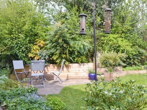 Een terras met twee stoelen, een houten muur en een tuin met diverse planten.
