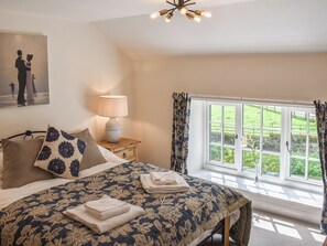 A bedroom with a bed, a nightstand, a lamp, a window with curtains, and a painting on the wall. - Keldholme Cottage 1 - UK10992 (Keldholme, near Kirkbymoorside)