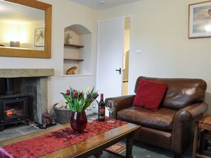 A cozy living room with a fireplace, a leather sofa, a red throw pillow, a vase with flowers, and a wine glass on a wooden table. - Keldholme Cottage 1 - UK10992 (Keldholme, near Kirkbymoorside)