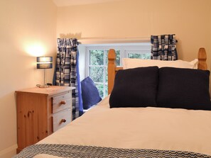 Une chambre à coucher avec un lit, une table de chevet, une lampe et une fenêtre avec des rideaux.