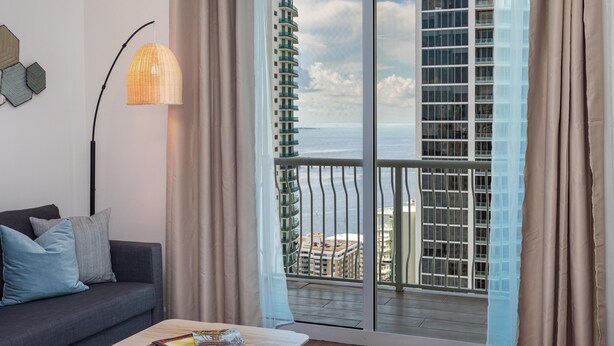 Un salon moderne avec un canapé, une lampe sur pied et une vue sur un immeuble de grande hauteur et la mer.