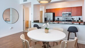 Une cuisine moderne dotée d’appareils électroménagers en acier inoxydable, une table de salle à manger ronde avec des chaises et un luminaire suspendu.