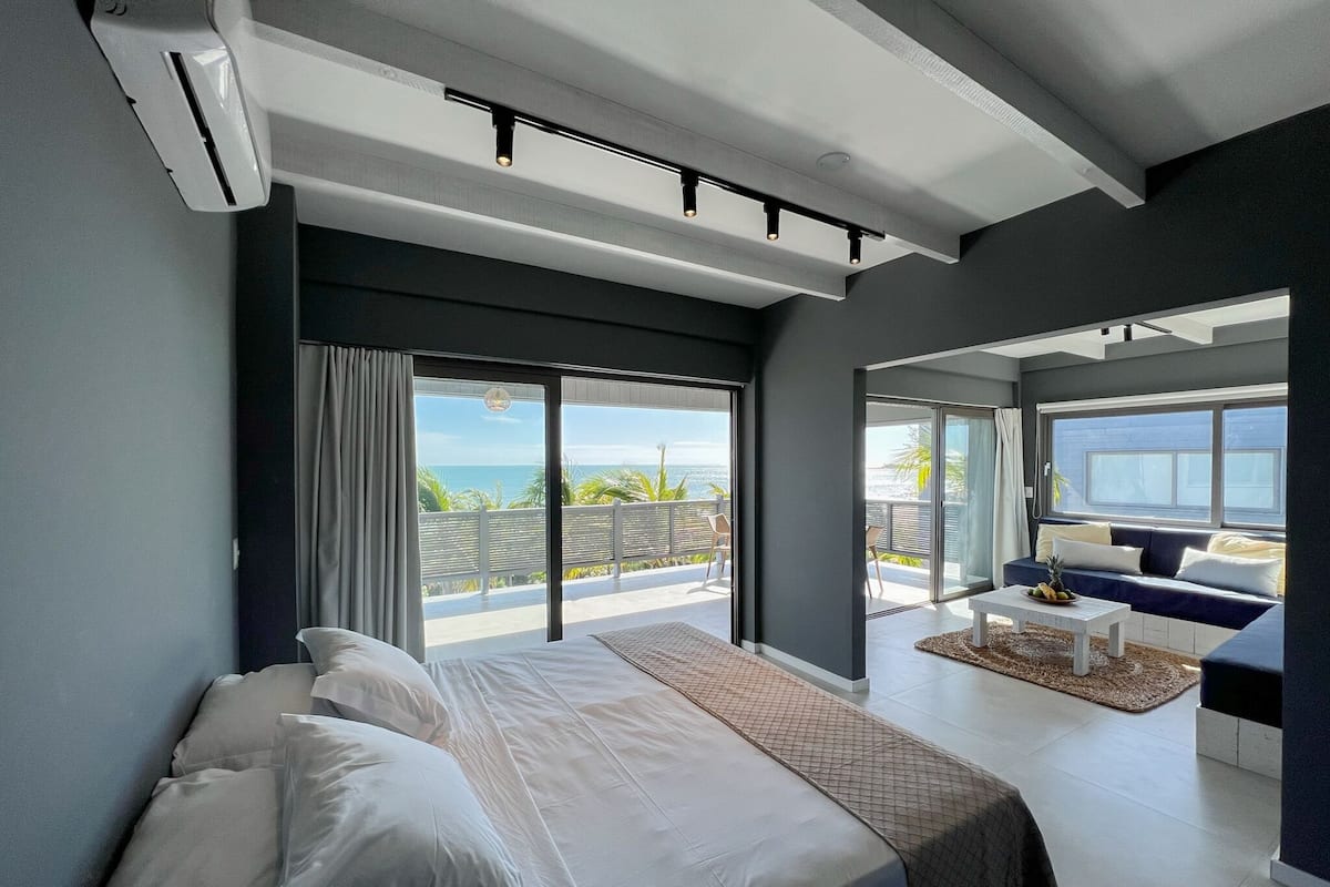 A modern bedroom with a large bed, a view of the ocean, and a balcony with a sofa.