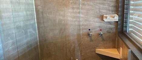 A modern bathroom with a glass-enclosed shower, a toilet, and a window with blinds.