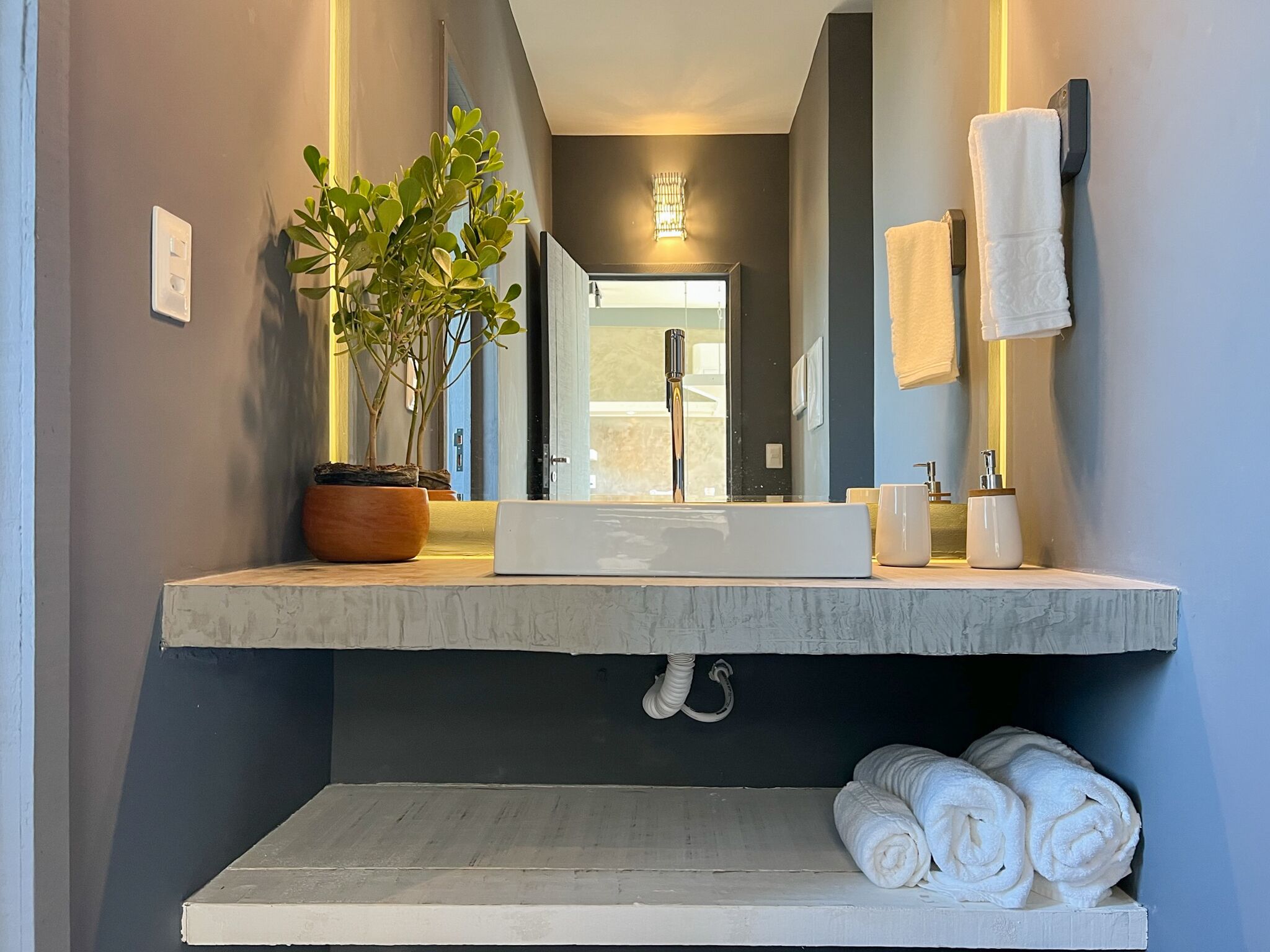 A modern bathroom with a large mirror, white sink, and a potted plant.