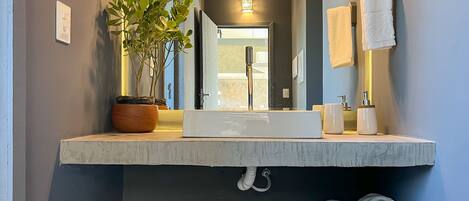A modern bathroom with a large mirror, white sink, and a potted plant.