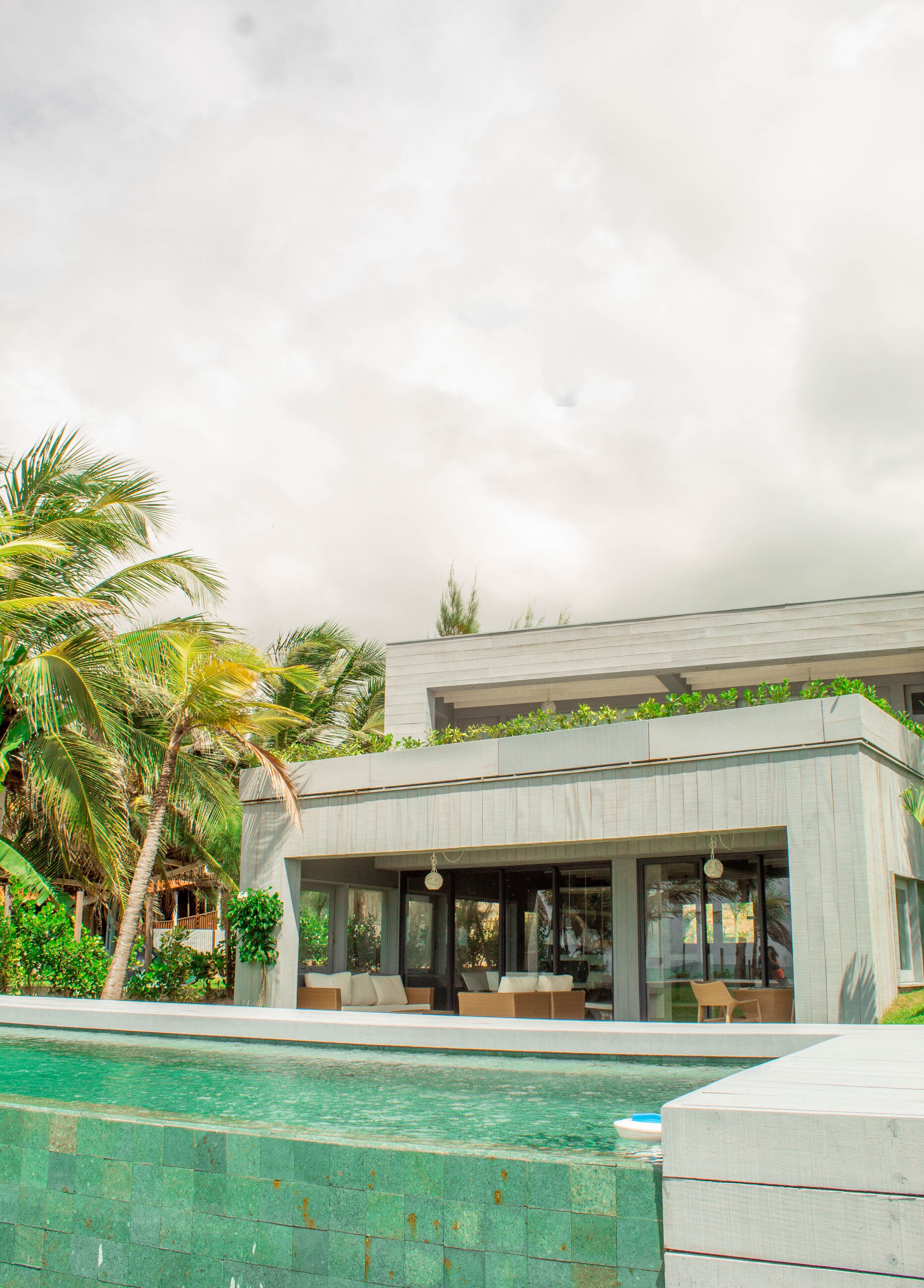 Un edificio moderno con piscina, rodeado de palmeras y follaje.