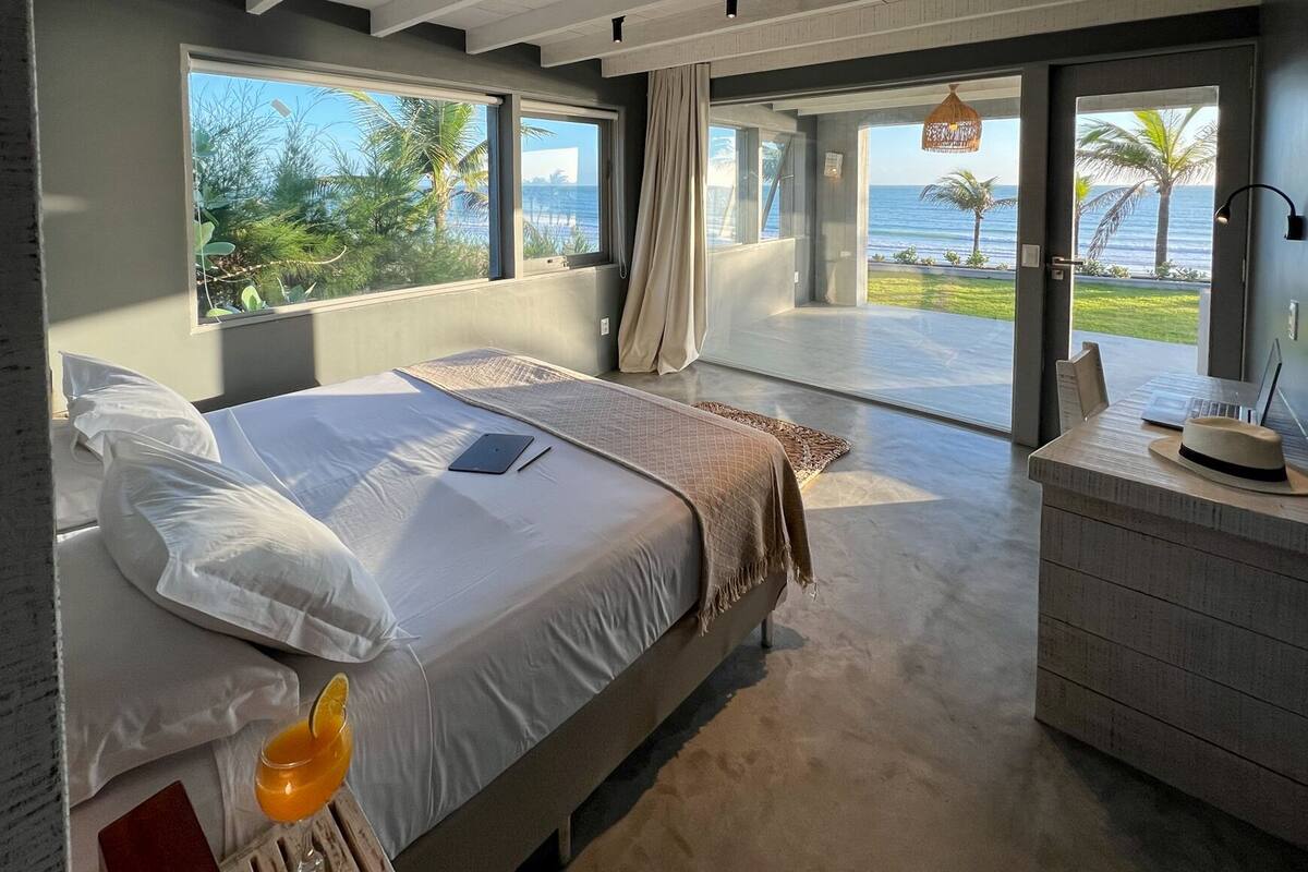 A bedroom with a bed, a desk, and a view of the ocean.