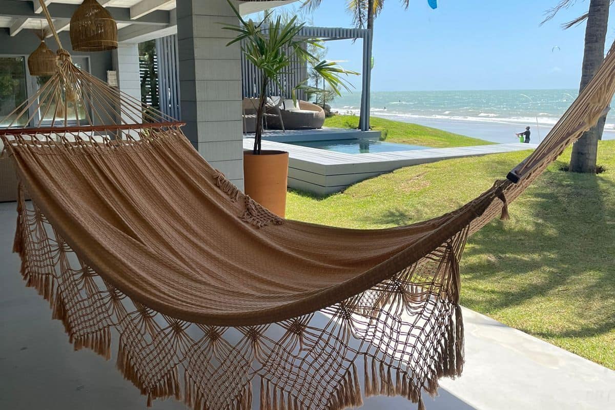 A hammock under a ceiling with hanging baskets, a pool, and a view of the ocean.