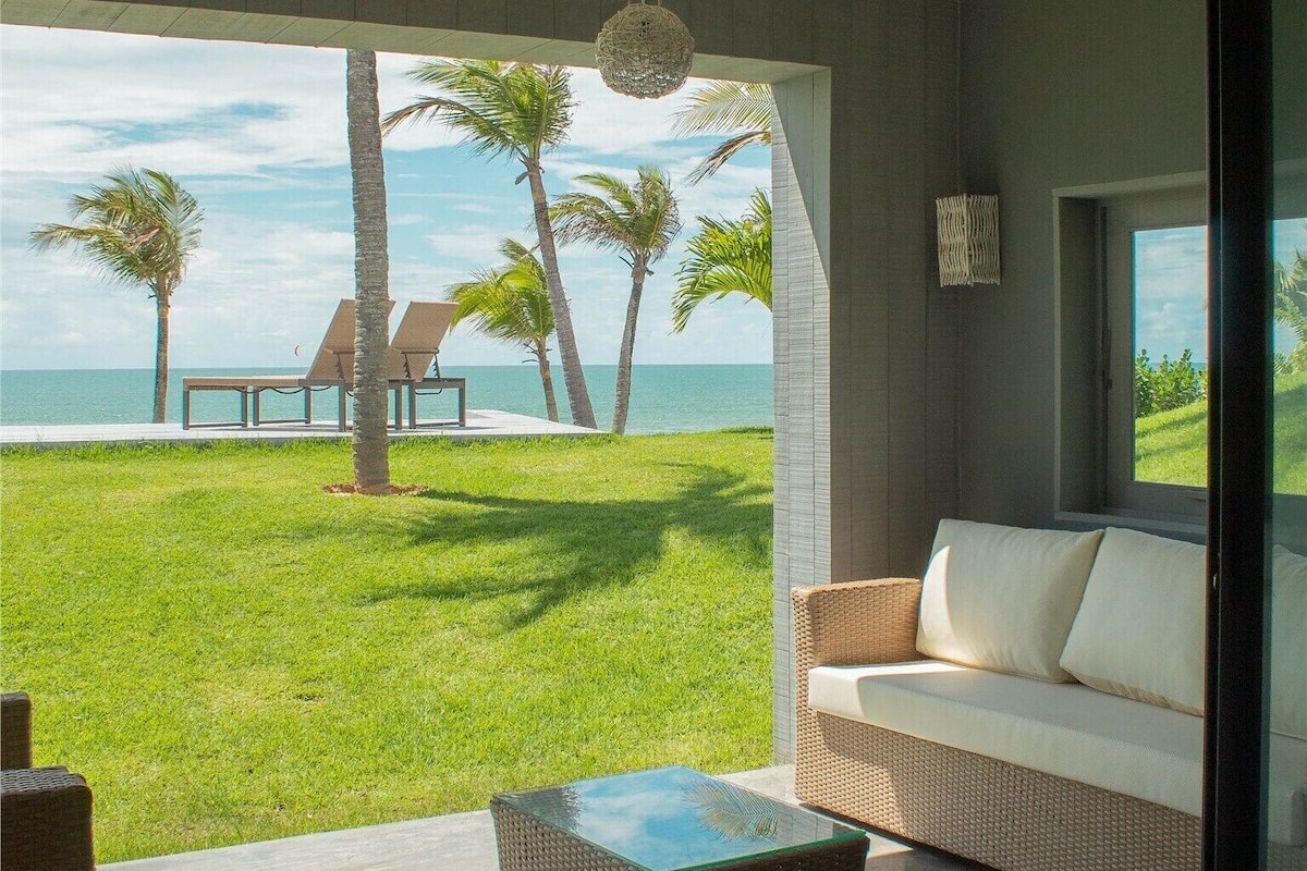 A room with a view of the ocean, a wicker sofa, a glass-top table, and a hanging light fixture.