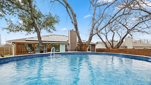 Piscina com deck de madeira e uma casa ao fundo.