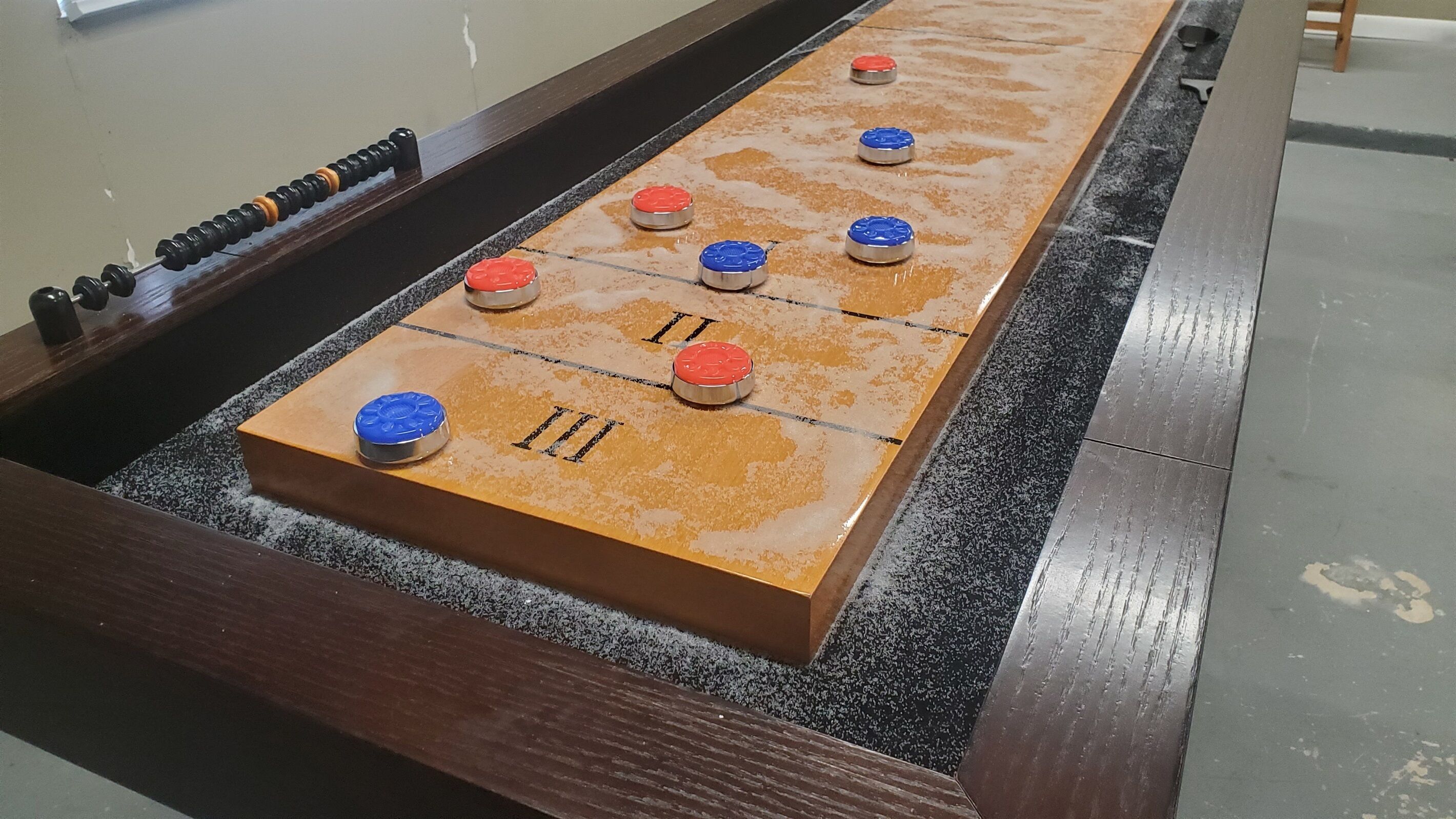 Uma mesa de futebol de botão com estrutura de madeira e superfície de jogo escura e texturizada.
