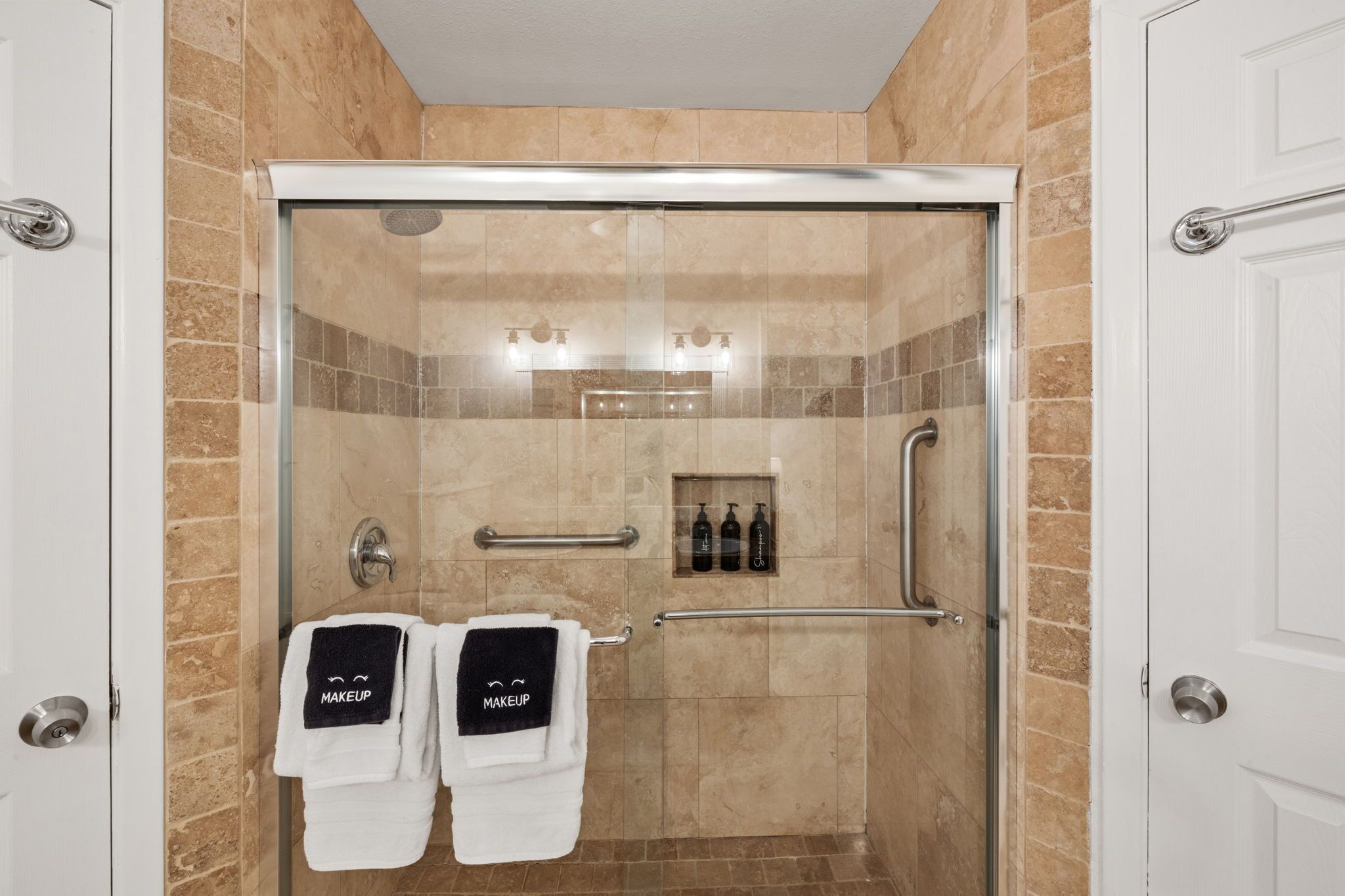Une douche fermée par des parois en verre, dotée d’un panneau de commande, d’un porte-serviettes avec des serviettes et d’une étagère contenant des articles de toilette.