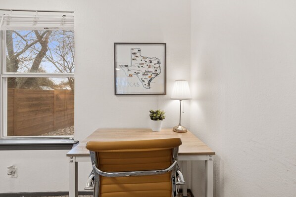 A room with a wooden desk, a brown leather chair, a framed map of Texas, a small potted plant, and a table lamp.