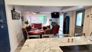 Uma cozinha com bancada de mármore, fogão por indução e uma área de jantar com mesa e cadeiras vermelhas.