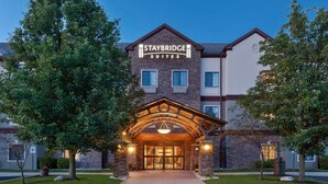 Entrada de um hotel Staybridge Suites com fachada de tijolos, janelas grandes e uma arcada convidativa.