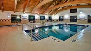 Een binnenzwembad met een houten plafond, vloertegels in ruitpatroon en duidelijke bewegwijzering voor badmeester en spa-faciliteiten.