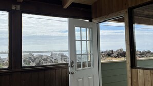 Puinen huone, jossa on kattovalokuvio, valkoinen ovi ja näkymä kivikkoiselle rantaviivalle.