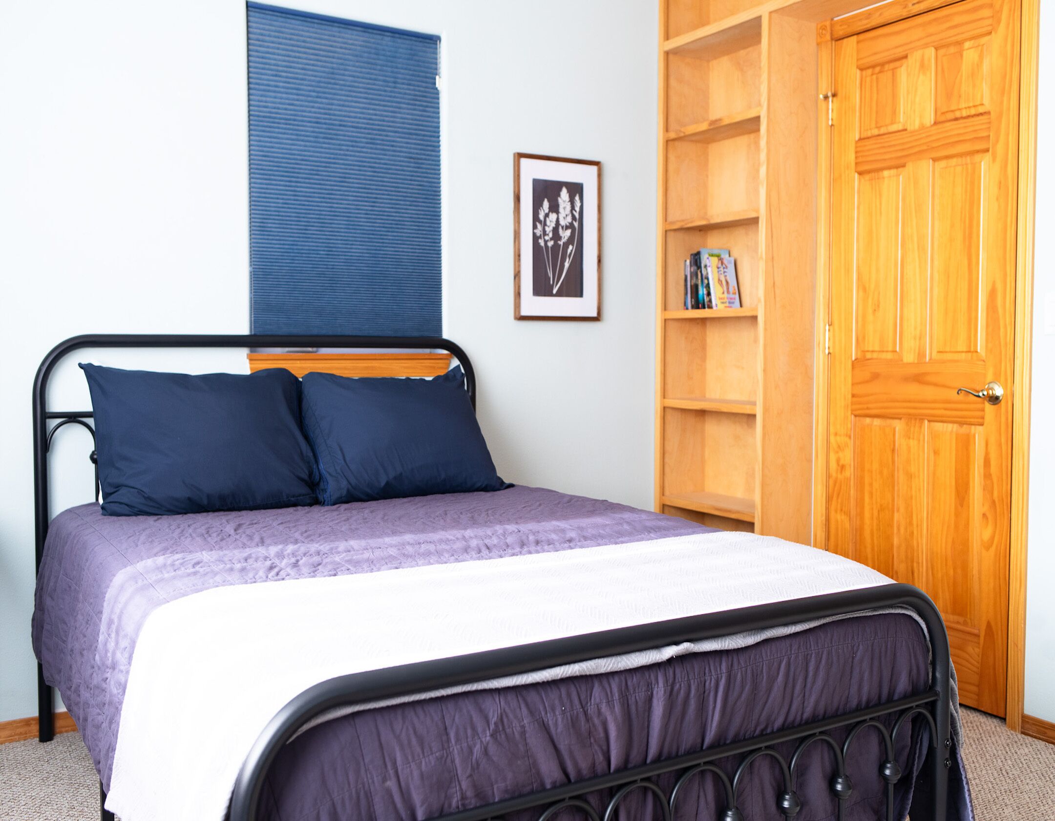 Une chambre à coucher avec un lit, une porte en bois, une bibliothèque et une fenêtre avec des stores.