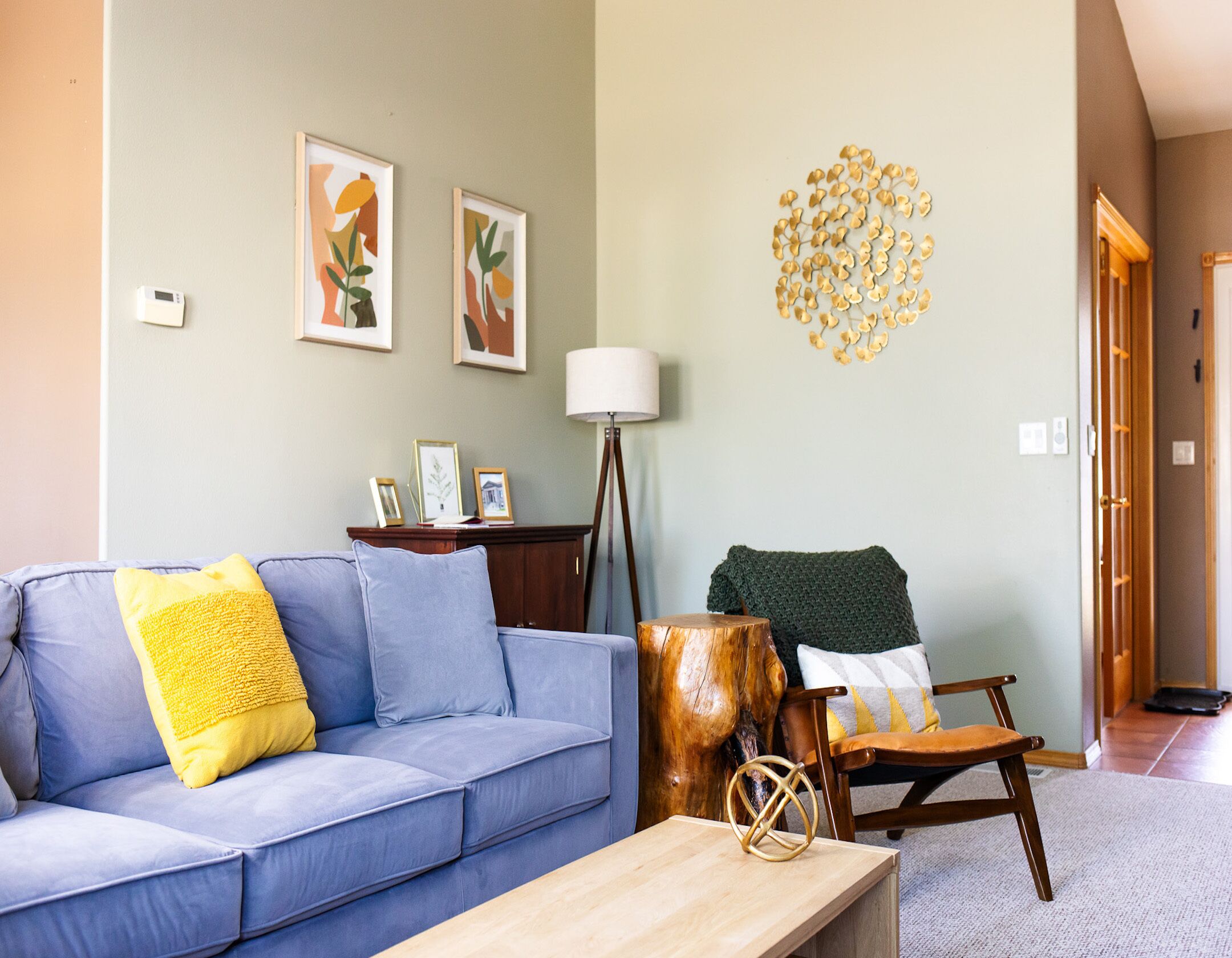 Un salon avec un canapé bleu, une table basse en bois, une chaise en bois et une lampe. Des tableaux encadrés ornent le mur, ainsi qu’un élément décoratif mural.