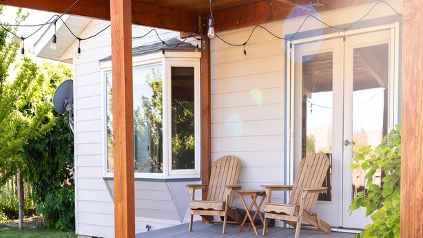 Eine überdachte Veranda mit zwei Holzstühlen und einem kleinen Tisch, Holzbalken und einem Fenster.