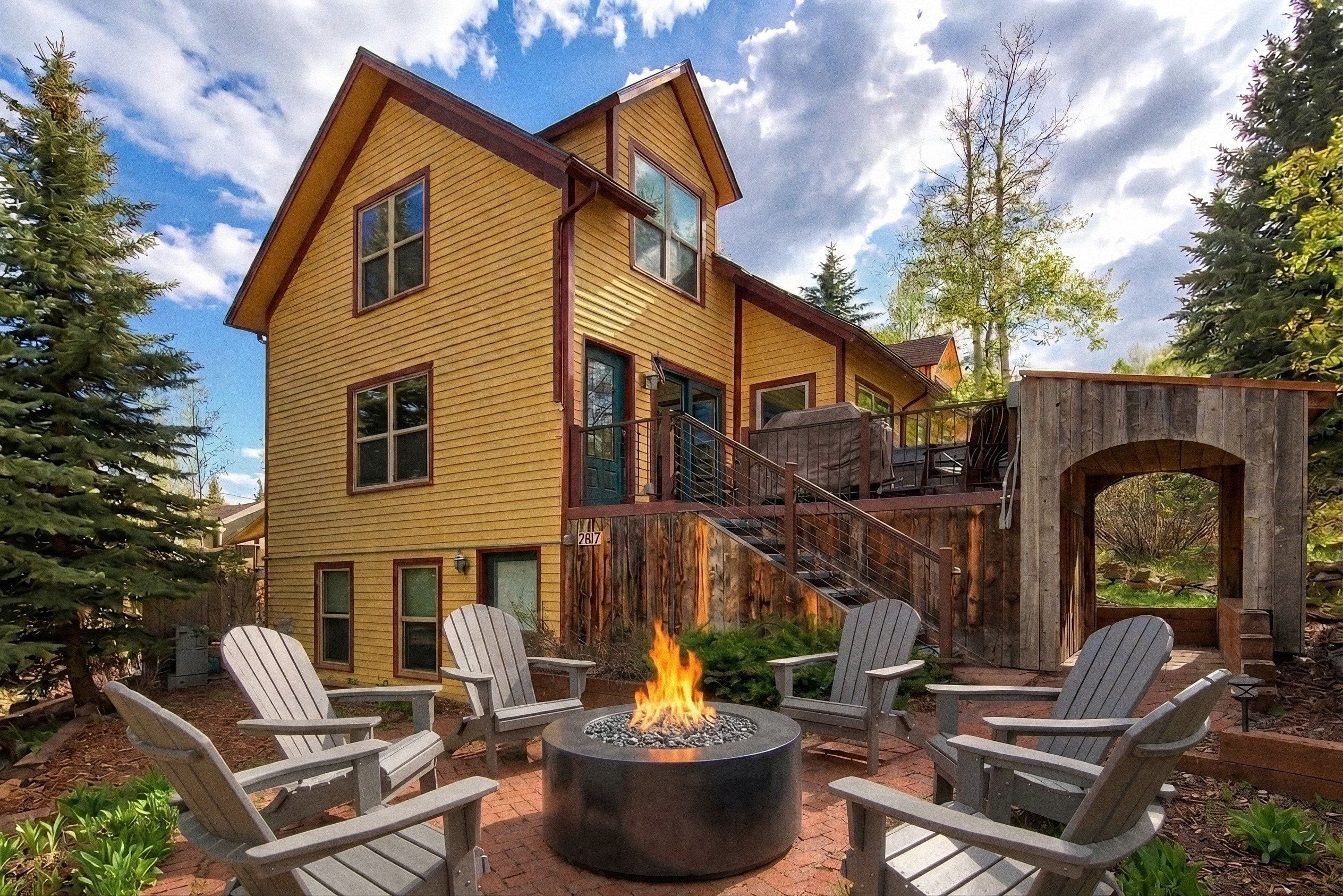 Une maison à deux étages avec un foyer au centre, entouré de fauteuils Adirondack.