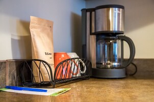 A kitchen counter with a coffee maker, a bag of coffee, a pair of glasses, and a red mug.