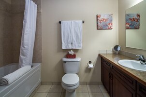 Un baño con bañera, inodoro, lavabo y dos espejos instalados en la pared.
