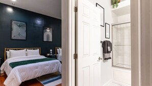 A hotel room with a bed, bedside tables, a dark wall with artwork, a white door, and a bathroom with a shower and tiled floor. - Jump right into the heart of Downtown Knoxville (Knoxville)