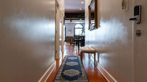 A hallway with wooden flooring, a blue and white patterned rug, and a door with a light switch and intercom on the wall. - Jump right into the heart of Downtown Knoxville (Knoxville)