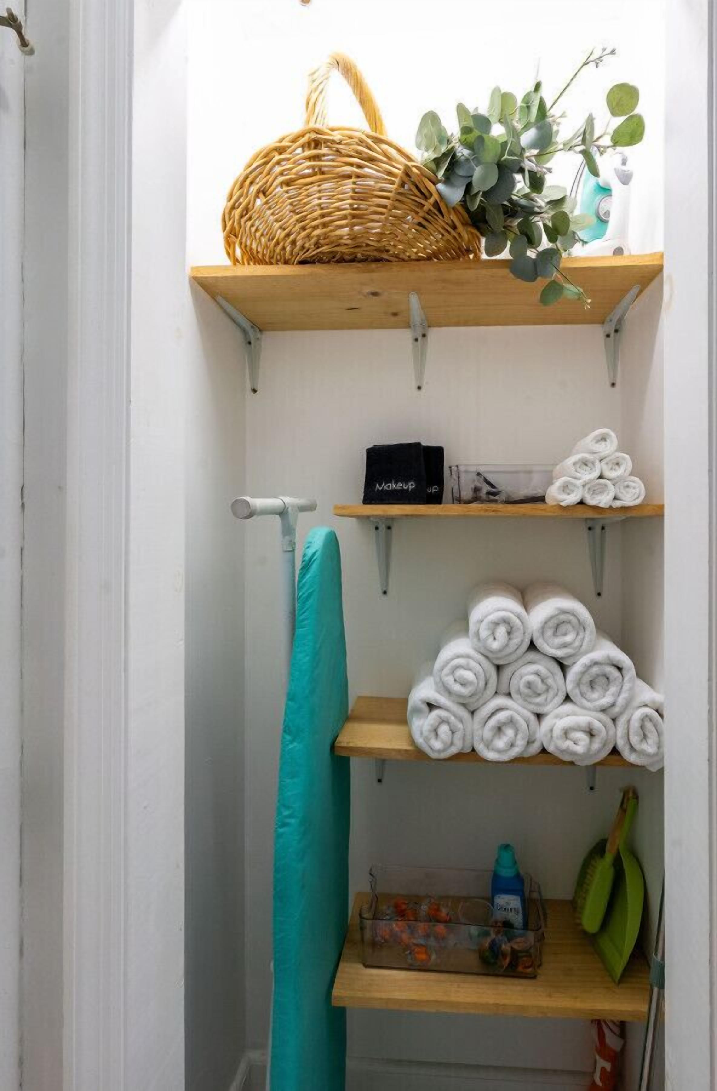 A bathroom with a wooden shelf holding a basket, a plant, and towels.