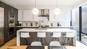 Una cucina moderna con isola centrale, sgabelli da bar, elettrodomestici in acciaio inossidabile e luci a sospensione.