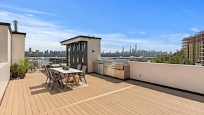 Una terrazza sul tetto con un tavolo e sedie, un barbecue e una piccola zona chiusa.